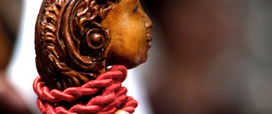Cabeza tallada en madera en el clavijero de un instrumento antiguo, con un cordón rojo
